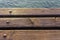 Wooden deck of a jetty in Lake Garda. The sun is reflected in the water. The wood is warm, brown in color. Detail, macro