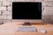 Wooden desk with computer, keyboard and mouse. Brick wall.