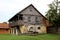 Wooden dilapidated old family house with stone foundation and large front balcony surrounded with uncut grass and well with hand