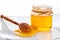 Wooden dipper next to jar of honey close-up on porcelain plate against white background