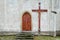 Wooden door to the church and a big cross on the wall. Lighted candles. Christian tradition.