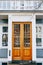 Wooden doors with blown glass in the building with white finishes and plastic windows with blinds, under a large balcony