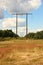 Wooden electrical tower in grass field with clouds