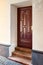 Wooden elegant entrance door with stone red granite threshold and steps at the facade of the building with peeling plaster