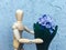 wooden faceless man gives blue flowers