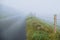 Wooden fence with barber wire and fog over small country asphalt road. Selective focus, dangerous driving conditions concept