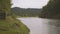 Wooden fence is on one side of large river, trees and mountain on other.