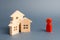 Wooden figures of houses and a red figure of the person on a gray background. Acquisition of real estate and assets.