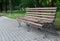 Wooden forged park bench, brown bench with forged metal legs, pavement tiles, park square