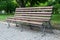 Wooden forged park bench, brown bench with forged metal legs, pavement tiles, park square
