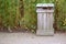 Wooden garbage bin near green plants