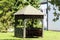 Wooden gazebo built from dilapidated wooden boards with new roof tiles on top surrounded with grass and trees