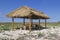 Wooden gazebo with a roof of reeds in the steppe. On the bench is a tourist backpack. Blue sky, steppe grass and flowers