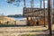 Wooden gazebo under reed roof with table in middle stand on shore of forest lake with sandy beach surrounded by pine trees against