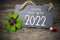 Wooden hang tag and slate with four leaf clover and sparklers with happy new year 2022 on wooden weathered background
