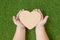 A wooden heart in the hands of a child against the background of a green grass.