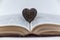 Wooden heart-shaped figurine. Large open book. Encyclopedia in red hardcover. Brown amulet with wood carving. Close-up. Selective