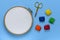 The wooden hoop with the white canvas, one metal scissors and five spools with colored threads are on the blue background, the