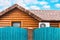 Wooden house with air conditioning, surrounded by a blue fence. Blue sky with clouds