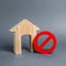 Wooden house figurine and a red prohibition symbol NO. Concept of inaccessibility or lack of housing. There is no opportunity