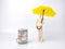 Wooden human mannequin holding a yellow umbrella near a roll of dollar bills on a white background