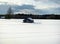 A wooden hut standing in the middle of white snowy field with pine trees in the background, hiding from snow, shelter,