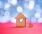Wooden icon of house with hole in the form of heart with little heart on red table with light bokeh background