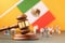 Wooden judge gavel, flag and plastic toy men on yellow background, Mexican society litigation concept