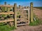 A wooden kissing gate gives access to a path along the edge of a field. Taken in a rural area in the north west of England.