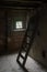 Wooden ladder illuminated by the light through a small window in the attic