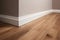 Wooden laminate flooring in a new house with white wall. Baseboard.