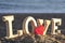 Wooden letters forming the word love with a red heart on the seashore. concept of lovers