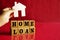 Wooden letters HOME LOAN with hand holding paper cut white home picture on a red background, financial concept