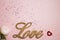 A wooden love letter with white flower red heart on pink glitter background.