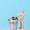 A wooden mannequin and coins in a miniature bucket on a blue background, a concept of high income, subsidy