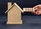 Wooden model of a house and a hand holds a block with an inscription  sale on a blue background. House sale concept, real estate