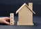 Wooden model of a house and a hand holds a block with an inscription  sale on a blue background. House sale concept, real estate
