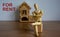 Wooden model of a sitting man in front of a miniature house. For rent inscription