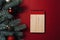 Wooden notebook on a red background next to New Year`s branches and decorations. Shopping and gifts list concept