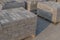 Wooden pallets standing not far to each other on cement surface, filled with gray fluted bricks for paving roads and sidewalks.