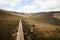 A wooden path in some irish green and brown hills with beautiful sky