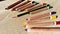 Wooden pencils of different colors lie on a beige table. Among them stands out one longer graphite pencil. Dissimilarity,