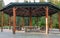 Wooden pergola in park with garden tables and chairs in the shadow. Wooden summerhouse is in a morning green park