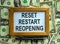 Wooden picture frame with inscription `reset restart reopening` on beautiful background from dollar bills and metalic pen. Conce