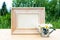 Wooden picture frame with miniature watering can and daisies outdoor in nature