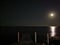 A wooden pier extending into the sea against a dark sky with the moon and a moon path