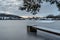 Wooden pier on lake with fresh snow.Winter pond with small jetty at sunrise,village in backround.Frosty calm landscape. White
