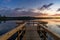 Wooden pier leads out onto a calm lake with forest on the opposite shore and a colorful sunset sky