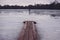 Wooden pier over a frozen lake in the woods. a fisherman is walking on the ice in the distance