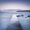 Wooden pier, rocks and sea on misty sunset.